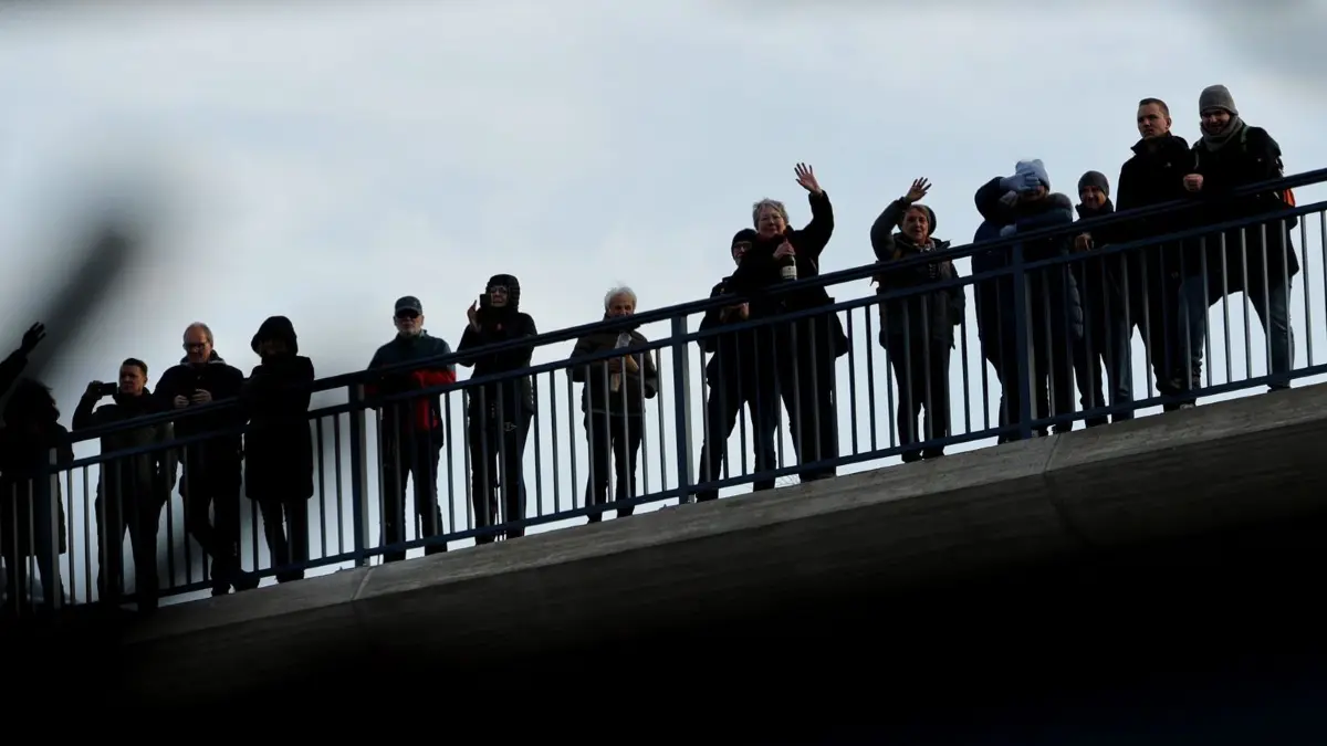Eröffnung der Rahmedetalbrücke: 22.12.2025, Nordrhein-Westfalen, Lüdenscheid: Schaulustige, die auf einer Brücke in der Nähe der Rahmedetalbrücke stehen, winken nach der Eröffnung einem Bus, der über die Brücke gefahren ist. Fast vier Jahren war im Sauerland die wichtige Nord-Süd-Achse A45 wegen einer maroden Brücke unterbrochen. Die marode Brücke war Anfang Dezember 2021 gesperrt und später gesprengt worden. Foto: Rolf Vennenbernd/dpa +++ dpa-Bildfunk +++