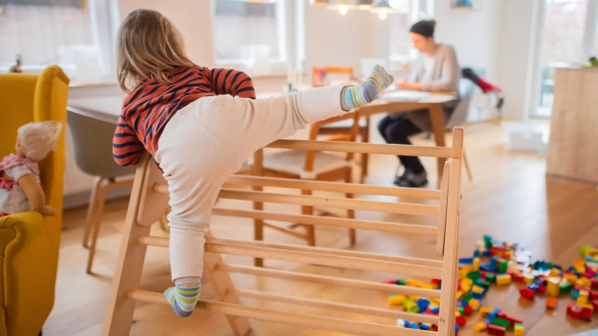Ein zweijähriges Kind klettert im Wohnzimmer auf ein Spielgerät: ILLUSTRATION - Das Wohnzimmer kann tagsüber Spielfläche und abends Rückzugsort sein: Flexible Raumgestaltung hilft, die Bedürfnisse von Kindern und Eltern zu vereinen. (zu dpa: «Spielen ums Sofa: So wird das Wohnzimmer familienfreundlich») Foto: Julian Stratenschulte/dpa/dpa-tmn - Honorarfrei nur für Bezieher des dpa-Themendienstes +++ dpa-Themendienst +++