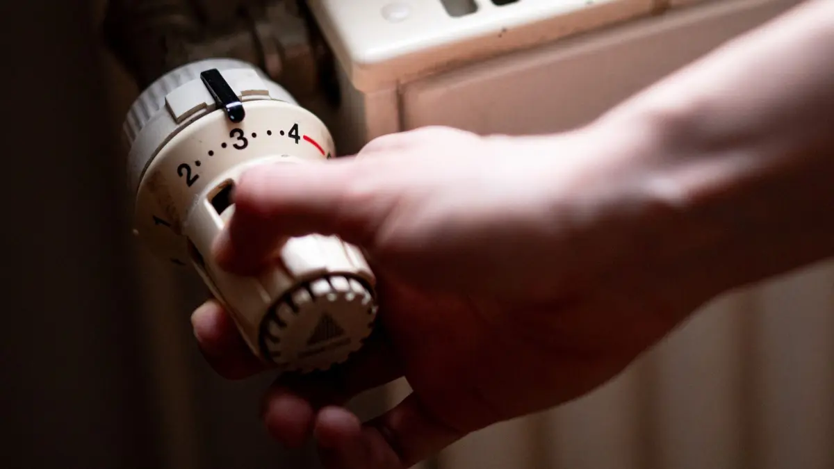 Heizkörper und Heizthermostat: ARCHIV - 02.07.2023, Berlin: Eine Person benutzt einen Heizkörper in einer Berliner Altbauwohnung. Laut Gebäudedienstleister Ista sind 2024 die Heizkosten in 70-Quadratmeter-Mietwohnungen bei Fernwärme um mehr als 27 Prozent gestiegen. (zu dpa: «Kälte und defekte Heizung: Unterricht fällt an Schule aus») Foto: Fabian Sommer/dpa +++ dpa-Bildfunk +++