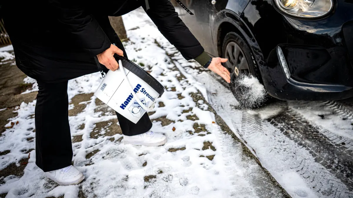 Winter in Niedersachsen: 07.01.2026, Niedersachsen, Verden: Eine Frau streut Salz vor ihr Auto, das wegen Glätte auf einer stark vereisten Straße feststeckt. Foto: Sina Schuldt/dpa +++ dpa-Bildfunk +++