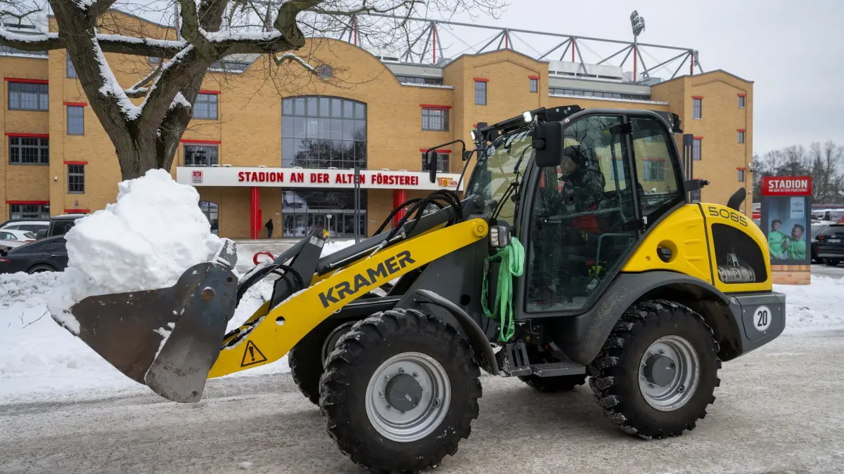 1. FC Union Winterdienst 2025/26: Fußball, Herren, Saison 2025/2026, 1. Bundesliga, 1. FC Union Berlin, freiwillige Fans und Angestellte befreien Wege und Parkplätze am und im Stadion An der Alten Försterei von Schnee, im Bild: ein Stadionmitarbeiter bringt mit einem Bagger Schnee weg, 08.01. 2026, Foto: Matthias Koch