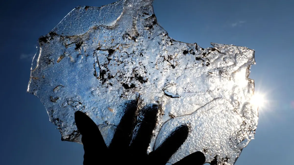 Eine Hand hält eine Eisplatte vor blauem Himmel
