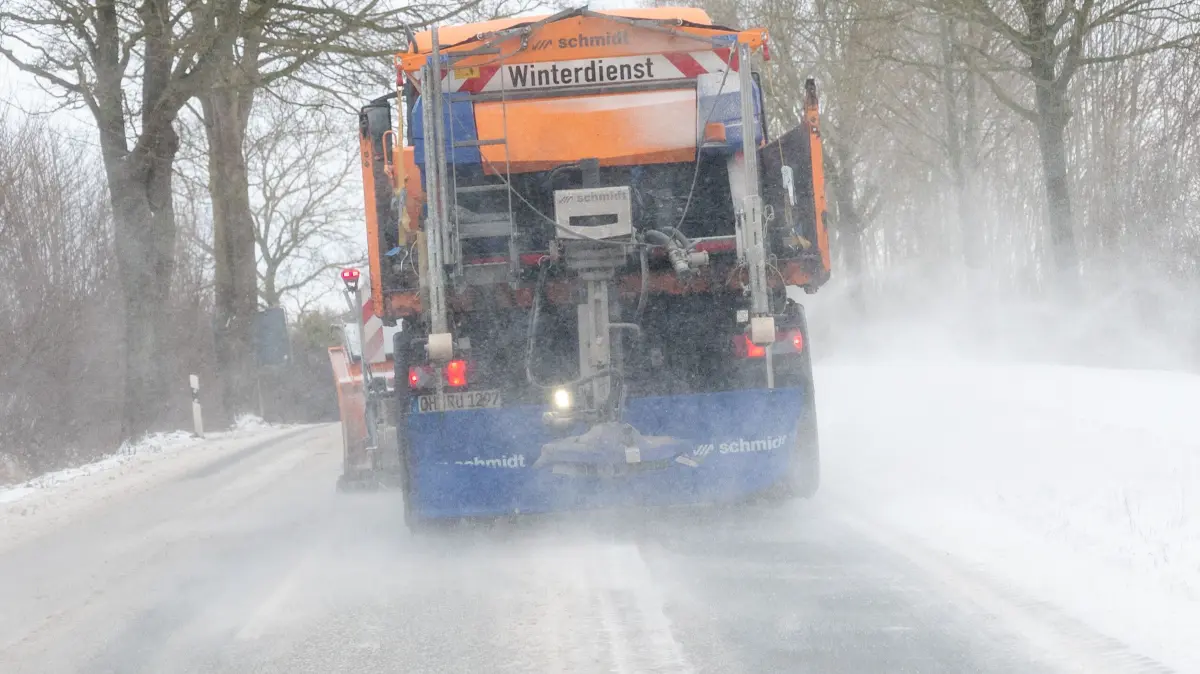 Ein Fahrzeug vom Winterdienst fährt bei Schneeverwehungen über eine Landstraße und räumt die Fahrbahn. +++ dpa-Bildfunk +++