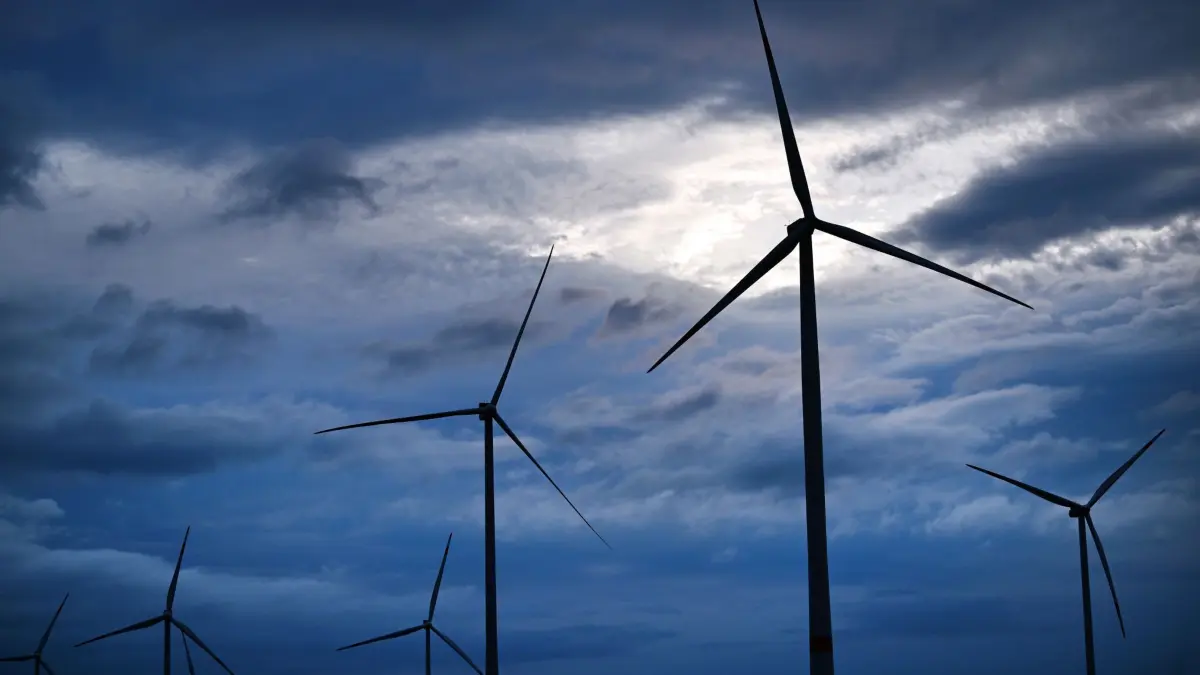 Windräder in Thüringen: ARCHIV - 31.07.2023, Thüringen, Warza: Sonnenlicht scheint zwischen dunklen Regenwolken hindurch über einem Windpark bei Gotha. (zu dpa: «Thüringen beim Windkraft-Ausbau weiter hinten») Foto: Martin Schutt/dpa +++ dpa-Bildfunk +++