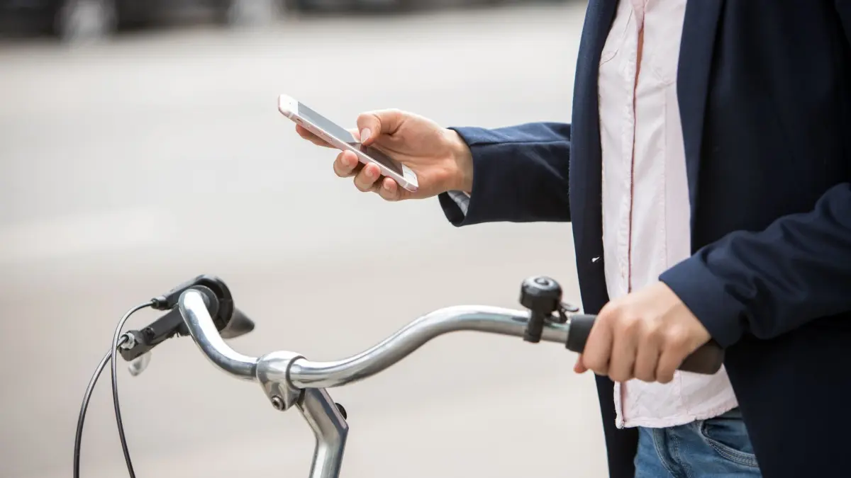 Eine Frau mit Smartphone und Fahrrad: ILLUSTRATION - Google Maps wird smarter: Der KI-Assistent Gemini unterstützt jetzt auch Fußgänger und Radfahrer bei der Navigation (zu dpa: «Google Maps: Gemini hilft Radfahrern und Fußgängern») Foto: Christin Klose/dpa-mag - Honorarfrei nur für Bezieher des Dienstes dpa-Magazin +++ dpa-Magazin +++