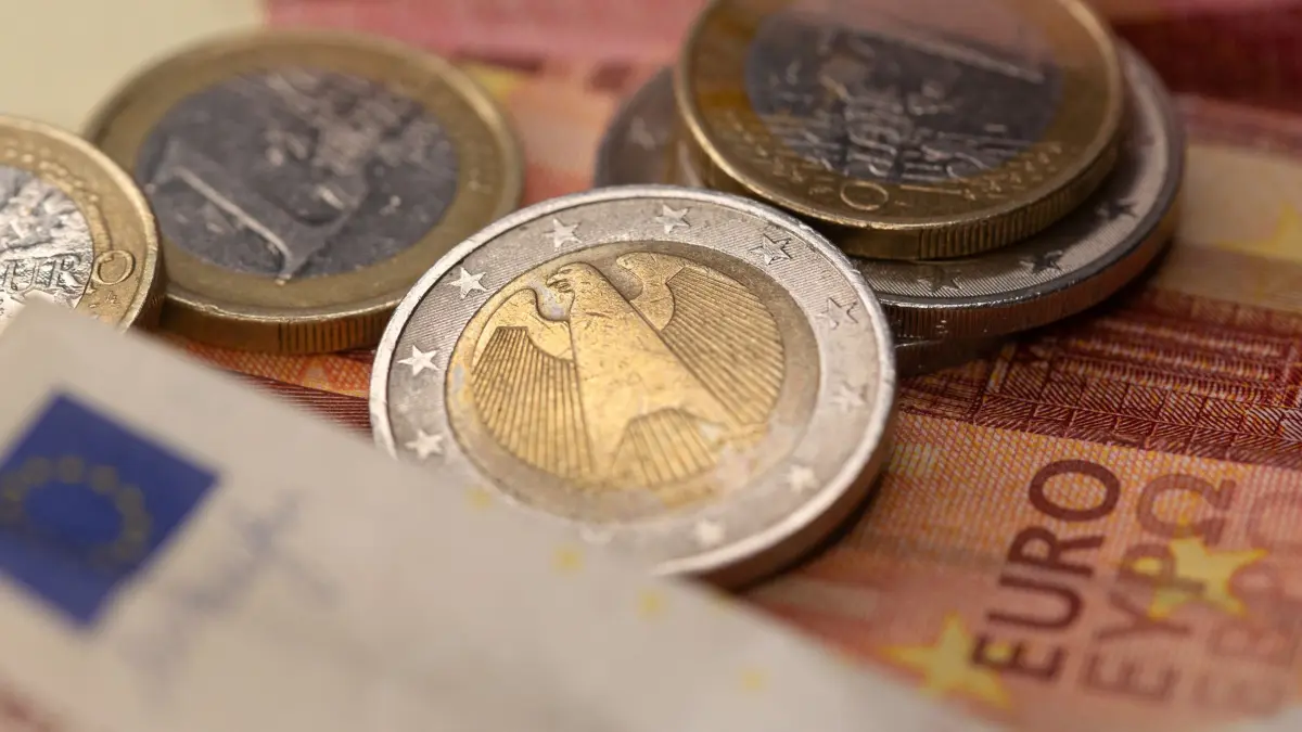 Geld - Euro-Münzen und Banknoten: ILLUSTRATION - 26.11.2025, Berlin: Münzen verschiedener Euro-Wertstufen liegen verstreut auf einem Tisch. Im Hintergrund sind Teile von Euro-Banknoten zu sehen. (zu dpa: «Eurokurs stabilisiert sich nach jüngsten Verlusten») Foto: Fernando Gutierrez-Juarez/dpa +++ dpa-Bildfunk +++