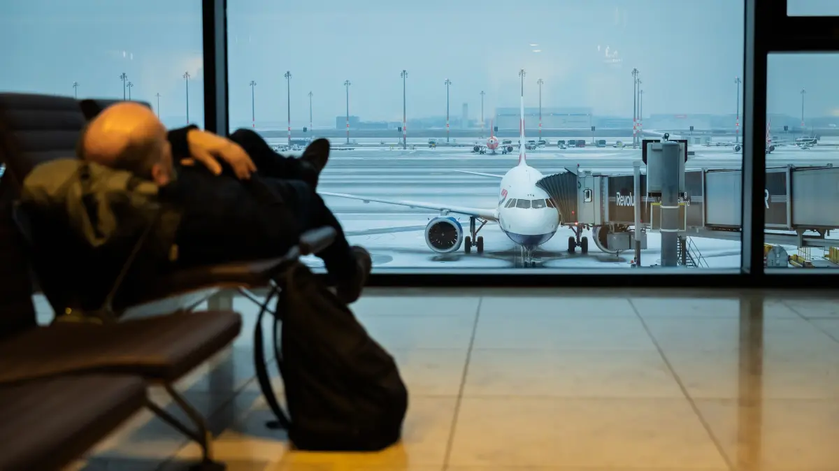 Ein Mann liegt mit Sicht auf den schneebedeckten Hauptstadtflughafen BER im Terminal. Am Flughafen BER ist der Flugverkehr aufgrund der Witterung eingestellt worden. +++ dpa-Bildfunk +++