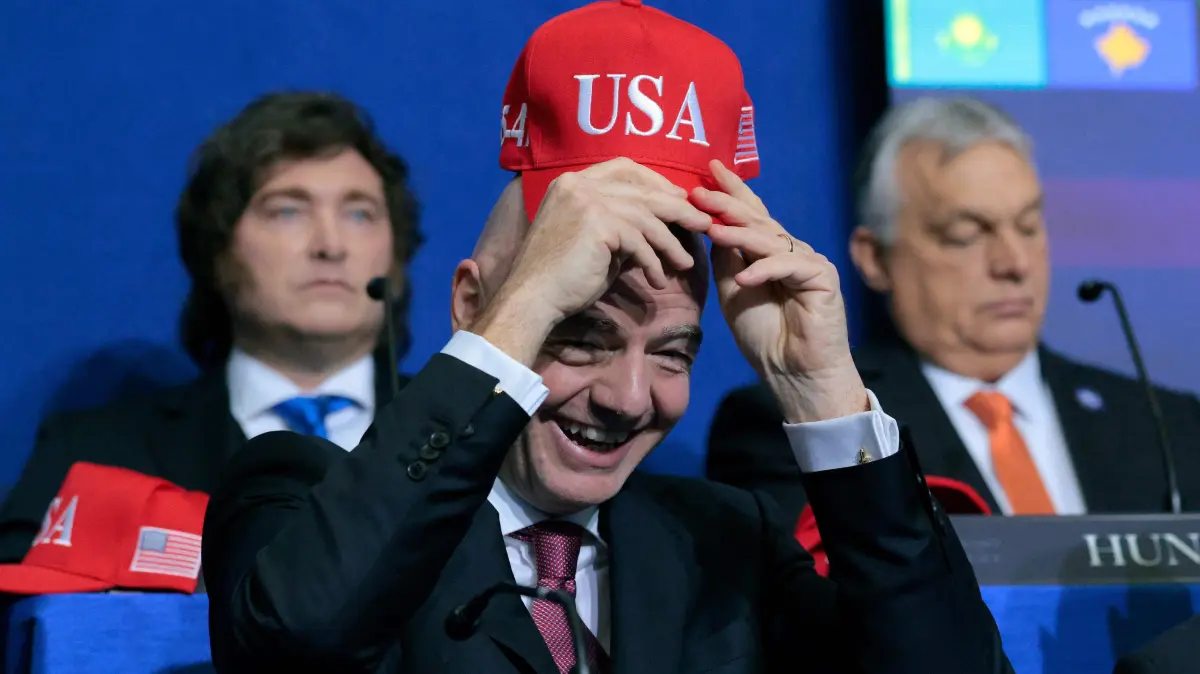 President Trump Convenes Board Of Peace's Inaugural Meeting: WASHINGTON, DC - FEBRUARY 19: President of FIFA Gianni Infantino holds up a USA hat as he attends the inaugural meeting of the Board of Peace at the Institute of Peace on February 19, 2026 in Washington, DC. Assembled to raise money for the rebuilding and stabilization of Gaza, Trump's Board of Peace was formally established on the sidelines of World Economic Forum in January of 2026. Chip Somodevilla/Getty Images/AFP (Photo by CHIP SOMODEVILLA / GETTY IMAGES NORTH AMERICA / Getty Images via AFP)