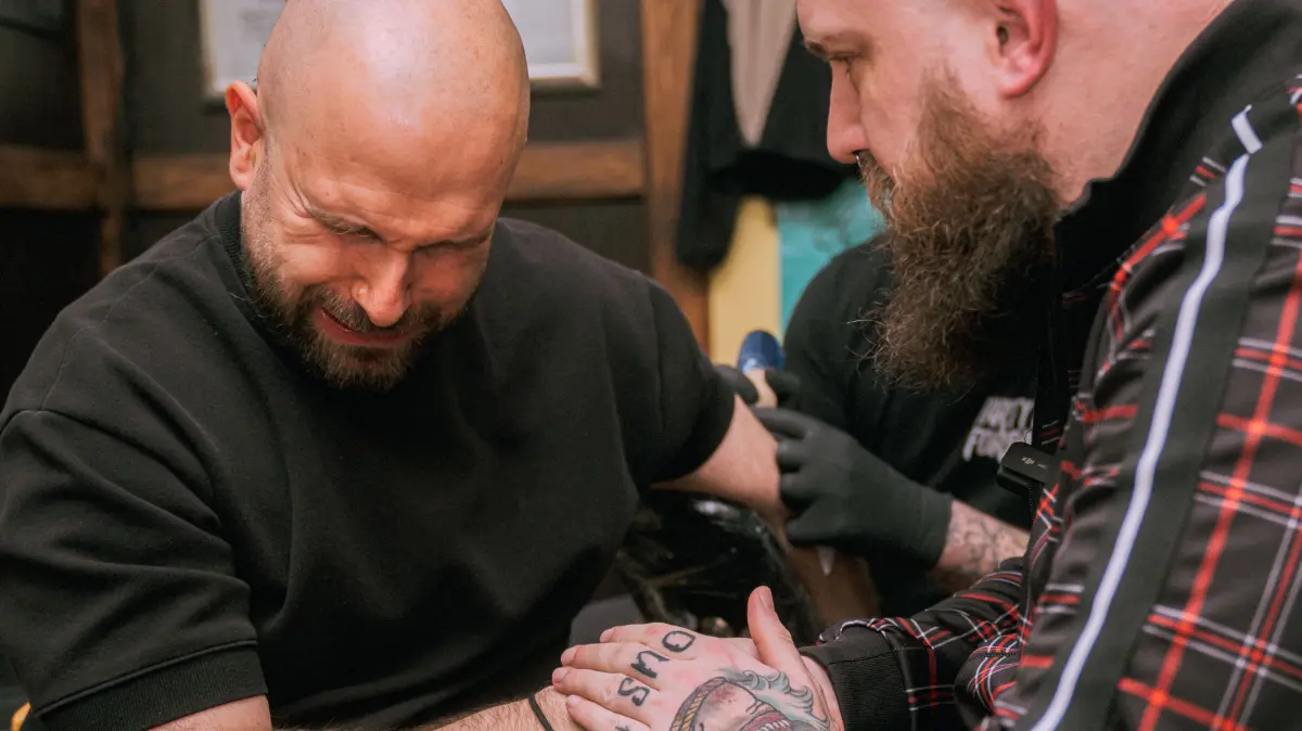 Dennis Baltzer bekommt auch selbst ein Tattoo. Social-Media-Manager Chris Büchler hält ihm die Hand.