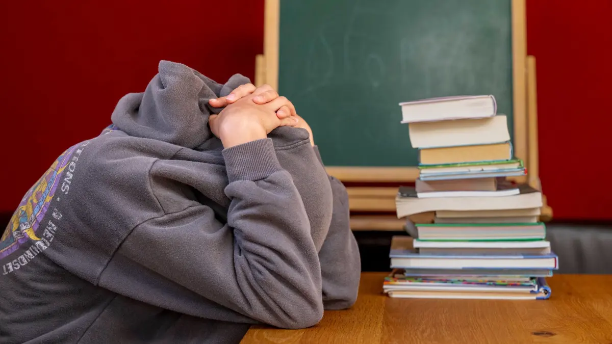 NRW startet großes Schüler-Feedback an allen Schulen: ARCHIV - 12.10.2022, Nordrhein-Westfalen, Rietberg: Eine Schülerin sitzt vor einem Stapel Büchern und hat die Kapuze ihres Pullovers über den Kopf gezogen. In Nordrhein-Westfalen soll systematisch erhoben werden, wie Kinder und Jugendliche sich an ihren Schulen fühlen und ob sie über das Schulleben mitentscheiden dürfen. (zu dpa: «NRW startet großes Schüler-Feedback an allen Schulen») Foto: David Inderlied/dpa +++ dpa-Bildfunk +++