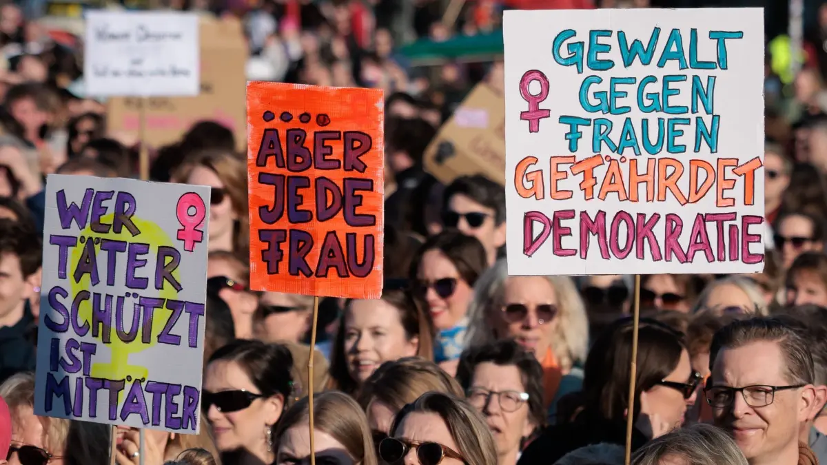 Demonstration gegen sexualisierte digitale Gewalt: 22.03.2026, Berlin: Teilnehmerinnen halten Schilder mit der Aufschrift «Wer Täter schützt ist Mittäter» (l-r), «Aber Jede Frau» und «Gewalt gegen Frauen gefährdet Demokratie» bei einer Demonstration gegen sexualisierte digitale Gewalt vor dem Brandenburger Tor. Foto: Carsten Koall/dpa +++ dpa-Bildfunk +++