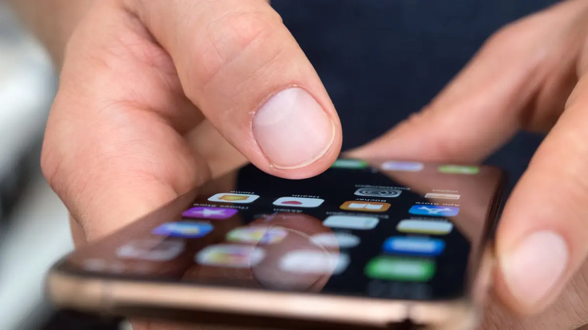 Ein Mann benutzt ein iPhone: ILLUSTRATION - Wer noch iOS 18.4 bis 18.7 nutzt, ist durch die Malware «Darksword» gefährdet. Doch auch ältere iPhones lassen sich mit einem Update schützen. (zu dpa: «So schützen Sie Ihr iPhone - vor der neuen Malware Darksword») Foto: Andrea Warnecke/dpa-tmn - Honorarfrei nur für Bezieher des dpa-Themendienstes +++ dpa-Themendienst +++