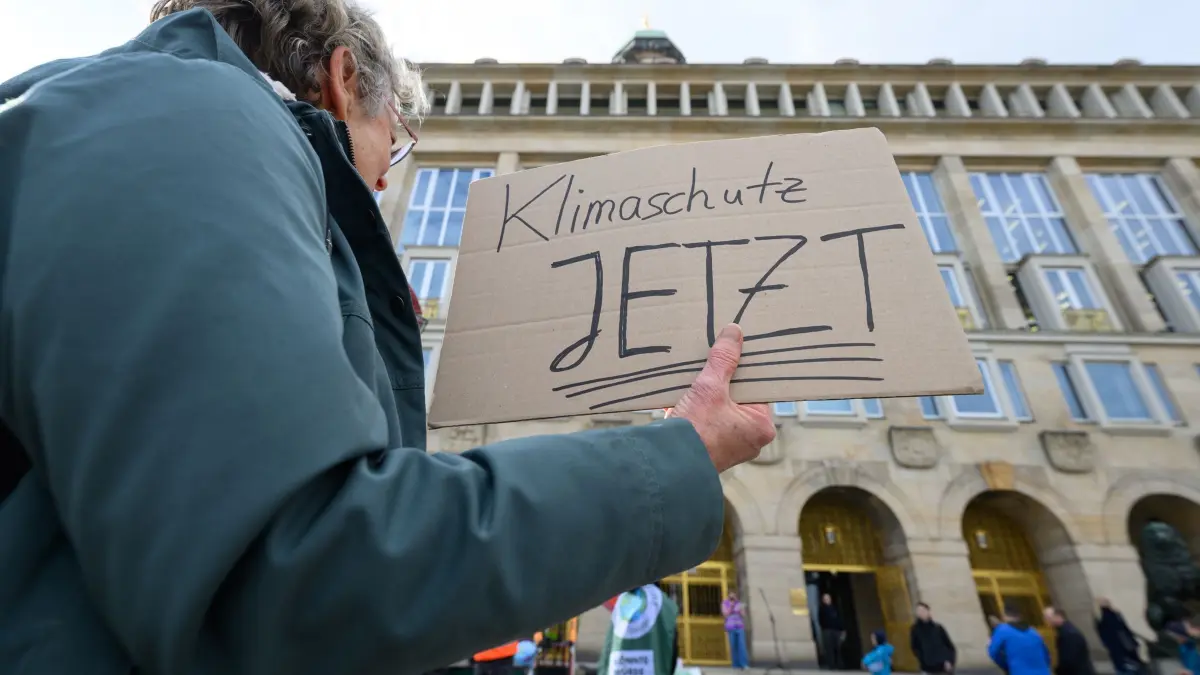 Klimademonstration in Dresden: 26.03.2026, Sachsen, Dresden: Eine Teilnehmerin eines breiten Bündnisses aus Umweltorganisationen, Wissenschaft und Jugendinitiativen hält bei einer Demonstration vor dem Rathaus ein Schild mit der Aufschrift „Klimaschutz jetzt“ in der Hand. Gemeinsam fordern die Teilnehmer verbindliche Klimaziele mit einem klaren Maßnahmenplan, einen konkreten kommunalen Ausstiegsplan aus der Gasnutzung sowie die Einrichtung eines Klimabeirats. Foto: Robert Michael/dpa +++ dpa-Bildfunk +++