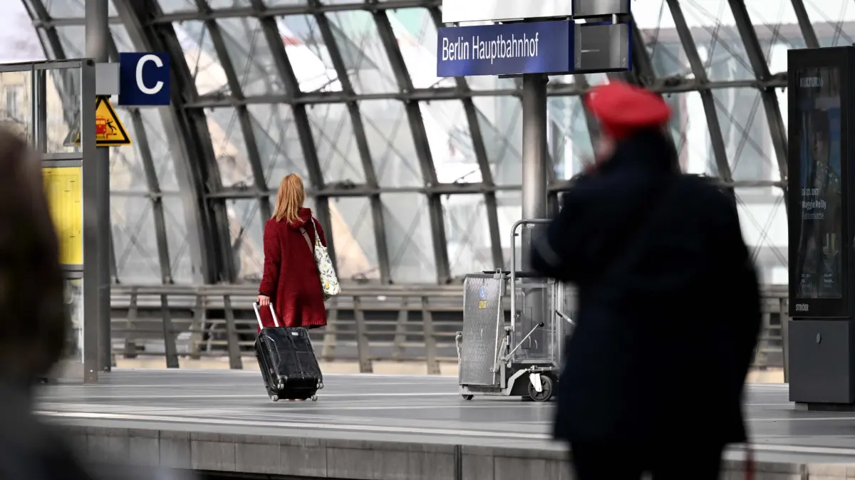 A traveller with suitcase and a train conductor walk along a platform at the main train station (Hauptbahnhof) in Berlin on March 27, 2026. Germany's beleaguered state railway Deutsche Bahn said on March 27 that its losses widened in 2025, weighed down by a write-off at its notoriously unpunctual long-distance division. (Photo by RALF HIRSCHBERGER / AFP)