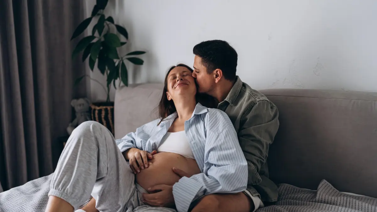 Eine schwangere Frau liegt mit ihrem Partner kuschelnd im Bett