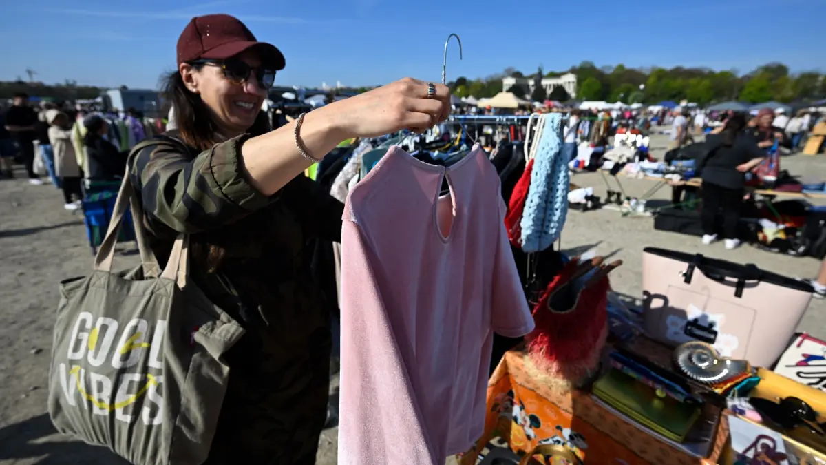 Münchner Frühlingsfest mit großem Flohmarkt: 18.04.2026, Bayern, München: Sandra Müller betrachtet an einem Stand auf dem Flohmarkt des Deutschen Roten Kreuzes (DRK) auf der Theresienwiese ein Kleidungsstück. Foto: Felix Hörhager/dpa - ACHTUNG: Nur zur redaktionellen Verwendung im Zusammenhang mit der aktuellen Berichterstattung +++ dpa-Bildfunk +++