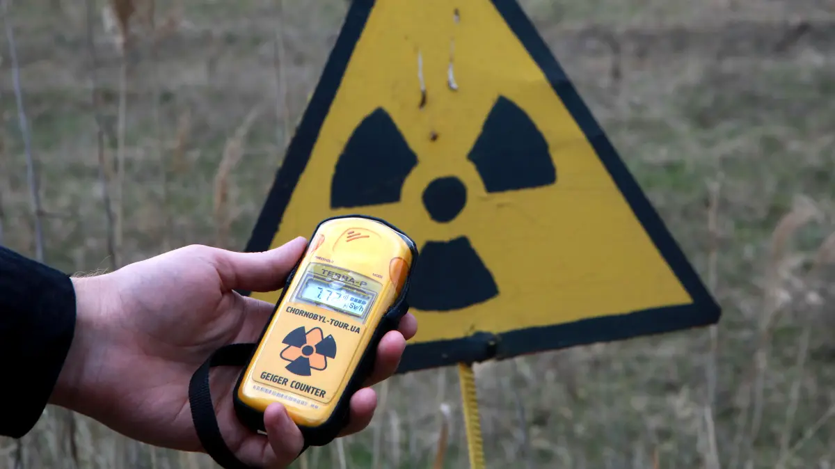 Eine Person hält einen Geigerzähler vor ein Warnschild in der heutigen Ukraine in der Nähe von Tschernobyl. Wie hoch war die Strahlung in der DDR? Jeder Soldat musste damals ein Messgerät tragen (Symbolbild)