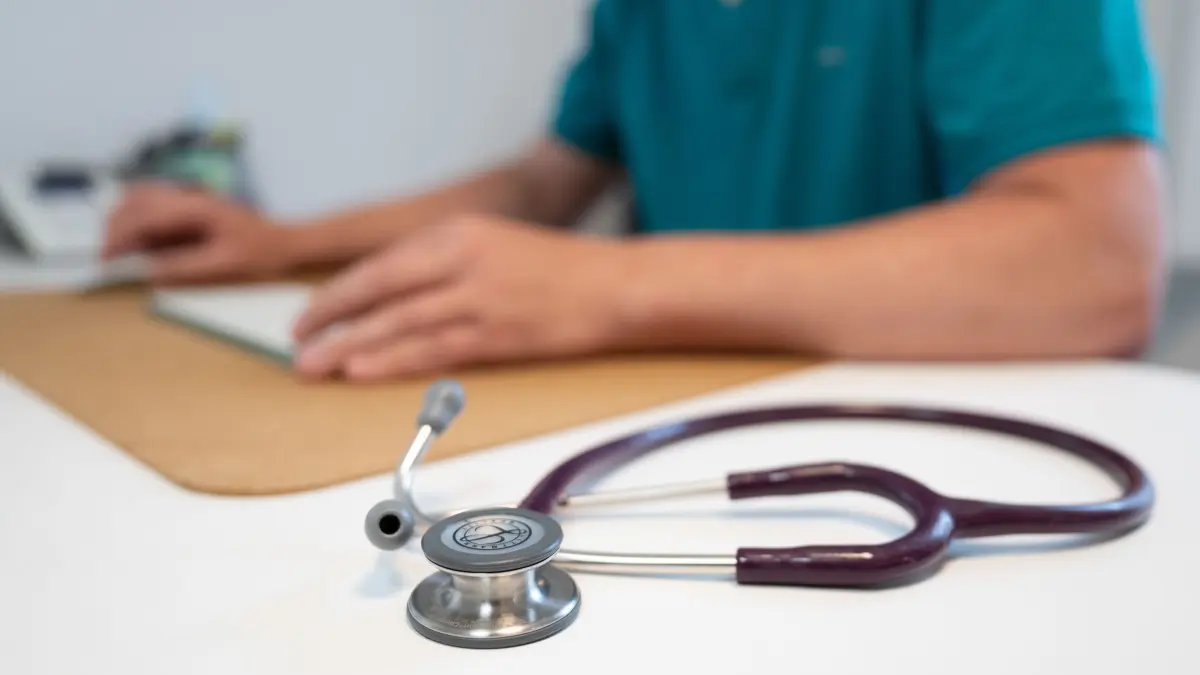 Arzt: ILLUSTRATION - 27.05.2025, Sachsen, Dresden: Ein Hausarzt sitzt in einem Sprechzimmer seiner Hausarztpraxis an einem Schreibtisch neben einem Stethoskop und arbeitet am Computer. (zu dpa: «Neue Handreichung für Ärzte zu Abbrüchen nach Vergewaltigung») Foto: Sebastian Kahnert/dpa +++ dpa-Bildfunk +++