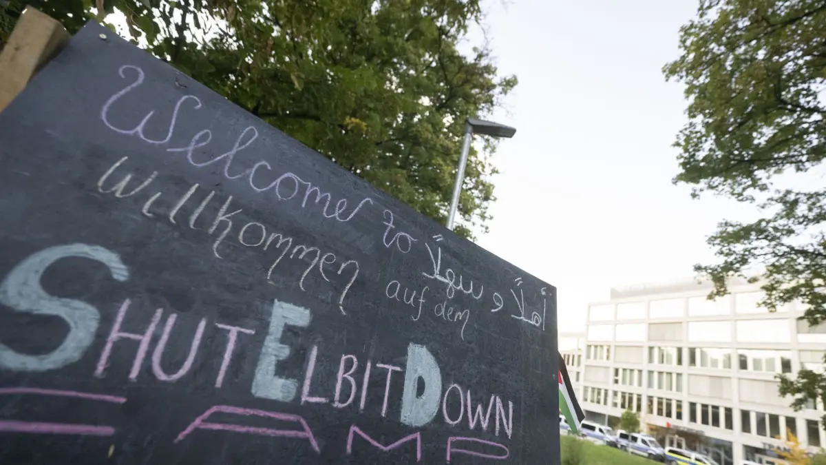 ARCHIV - 20.09.2025, Baden-Württemberg, Ulm: Ein Schild mit der Aufschrift «Willkommen auf dem ShutElbitDown Camp!» steht auf einem Protestcamp vor einem Bürogebäude, in dem sich unter anderem Räume des Rüstungskonzerns Elbit Systems befinden. (zu dpa: «Anklage nach Angriff auf israelischen Rüstungskonzern in Ulm») Foto: Marijan Murat/dpa +++ dpa-Bildfunk +++