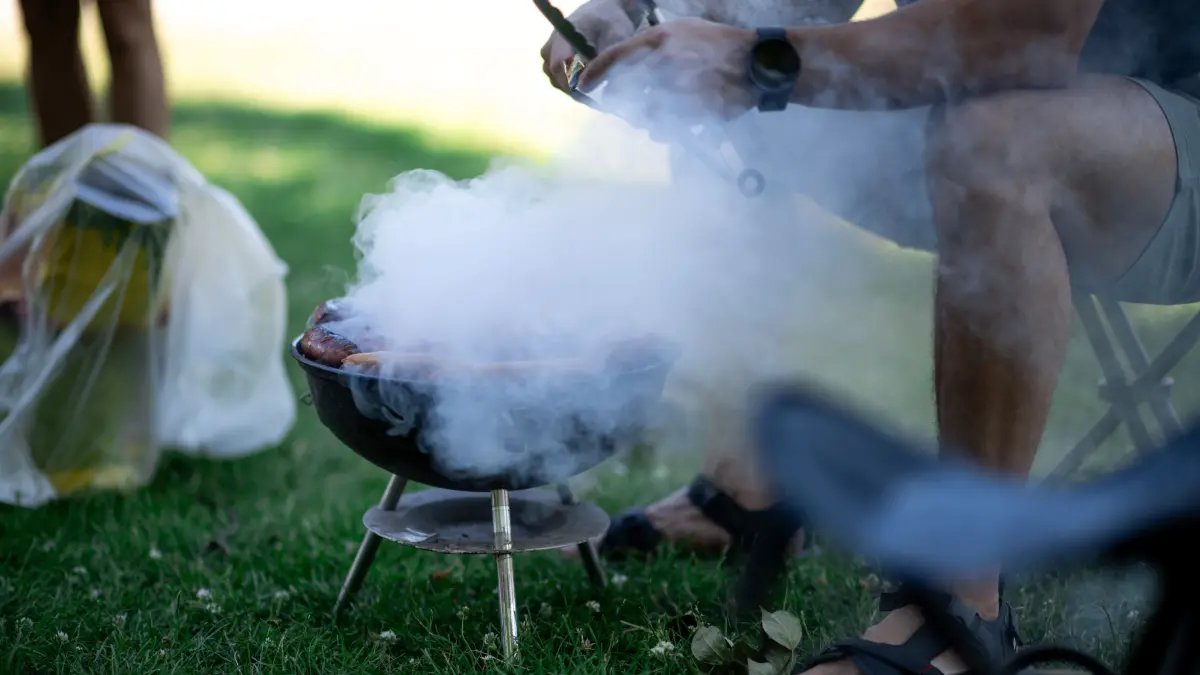 Ein Mann sitzt im Park am Aachener Weiher vor einem rauchenden Grill. (zu dpa: «Schwere Grillunfälle sind selten») +++ dpa-Bildfunk +++