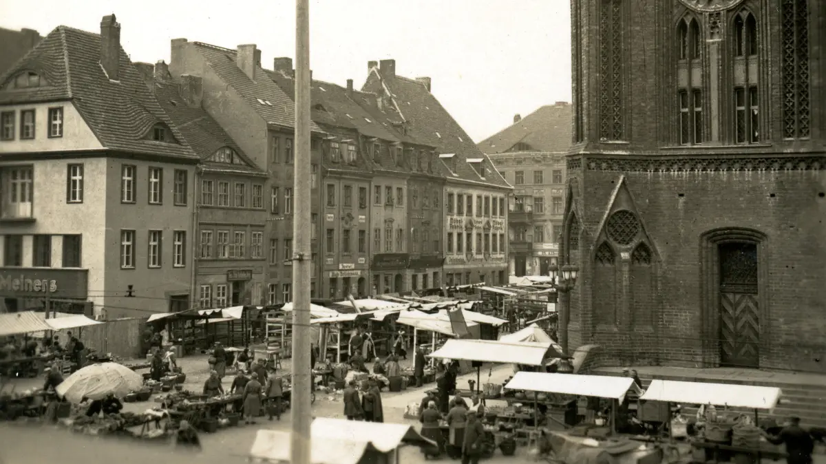 Impfen Historisch: Blick auf die Häuserreihe Sieben Raben beim Rathaus an einem Markttag im Frühjahr 1930. Das vierte Haus von links, in der Mitte der Häuserreihe, Große Scharrnstraße 66 bzw. Markt 4, besaß zu dieser Zeit der Tapeten- und Linoleumhändler Hugo Brückmann. Ein Jahrhundert zuvor gehörte es dem Stadt- und Amtschirurgen Johann Gottfried Simon (1768-1833), der hier in seinem Haus die Frankfurter gegen die Pocken impfte. Dieses Haus war Frankfurt erstes Impfzentrum.