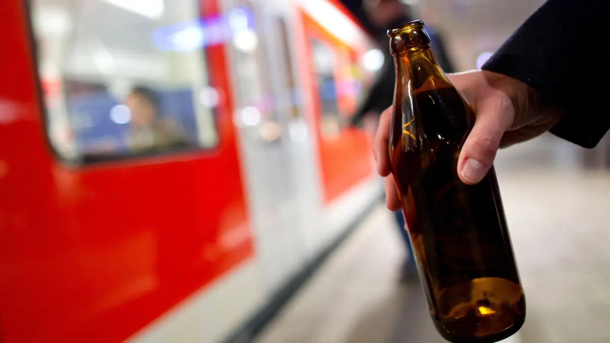 Eine Person hält auf einem Bahnsteig eine Bierflasche in der Hand. Seit dem 1. Mai gibt es in Berlin zwei Bahnhöfe an denen der Konsum von Alkohol verboten ist. Infrastrukturminister Robert Crumbach wünscht sich eine Debatte über ein generelles Alkoholverbot in Brandenburg. (Symbolbild)