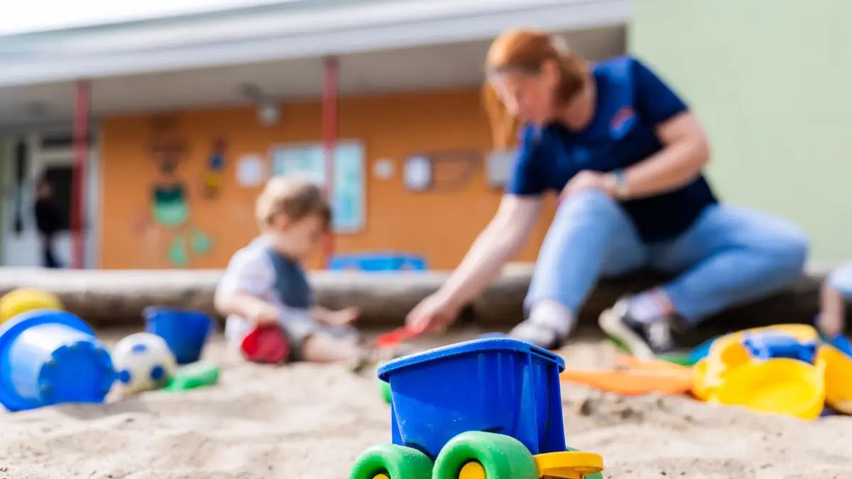 ARCHIV - 23.08.2024, Berlin: Ein Kind spielt mit einer Erzieherin im Sandkasten einer Kita. Die hochumstrittenen Lockerungen der Personalvorgaben in nordrhein-westfälischen Kitas können ab sofort umgesetzt werden. (zu dpa: «Umstrittene Kita-Personalverordnung in Kraft») Foto: Christoph Soeder/dpa +++ dpa-Bildfunk +++
