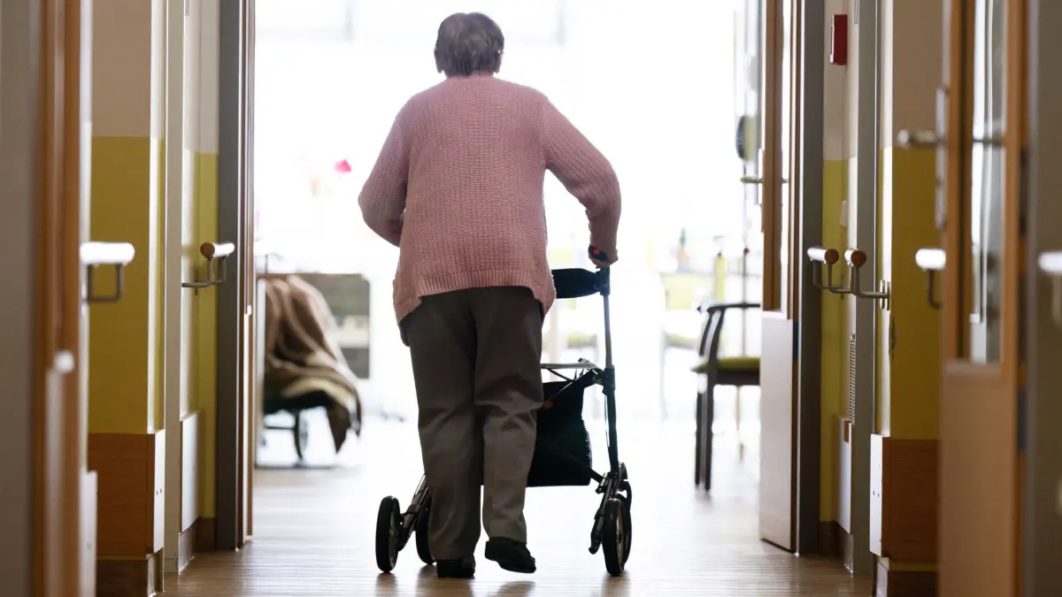 Pflegeheim: ARCHIV - 03.04.2025, Sachsen, Dresden: Eine Frau geht mit einem Rollator in einem Altenheim auf einem Gang entlang. (zu dpa: «Gewerkschaft kündigt für «Tag der Pflege» Proteste an») Foto: Sebastian Kahnert/dpa +++ dpa-Bildfunk +++