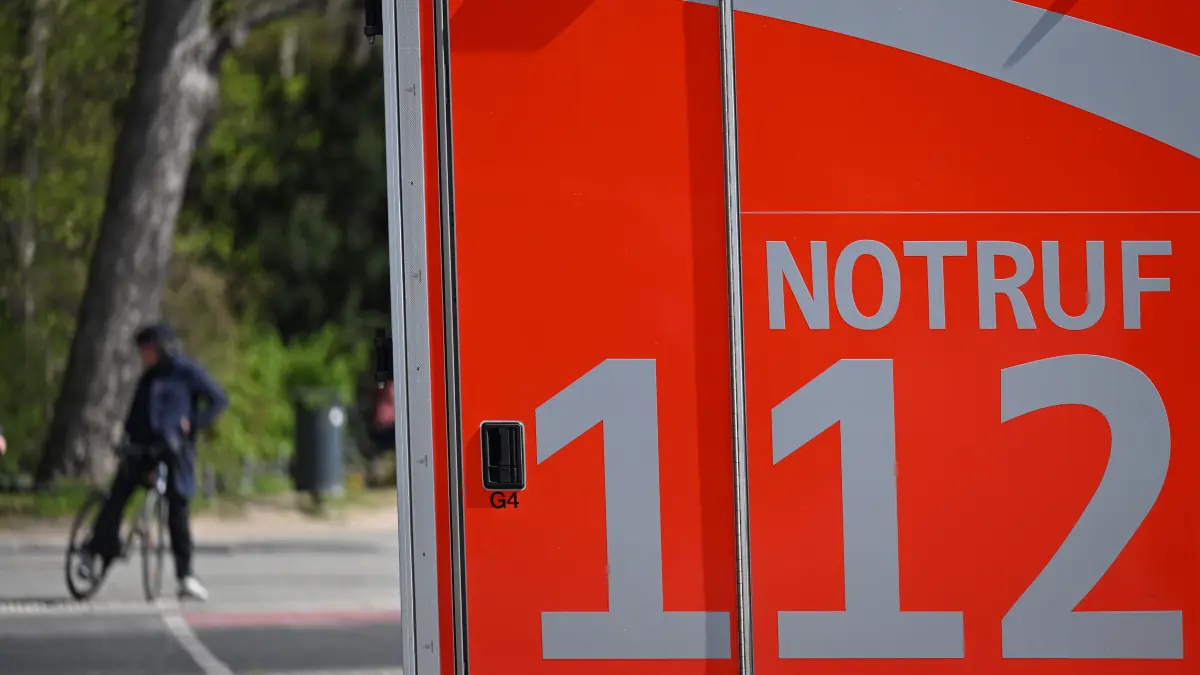 Ein Krankenwagen mit der Aufschrift „«Notruf 112“» fährt eine Straße entlang. Im Hintergrund ist eine Radfahrerin zu sehen. (zu dpa: «Kinder springen während Fahrt auf «Flotte Lotte»») +++ dpa-Bildfunk +++