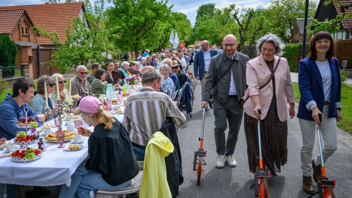 Längste Kaffeetafel im Oderbruch: 09.05.2026, Brandenburg, Wuschewier: Rene Wilke (SPD), Brandenburger Minister für Arbeit und Gesundheit, geht zusammen mit zwei weiteren Personen mit Geräten für die Längenmessung an einer Kaffeetafel entlang. Der Minister nahm als Teil einer Jury an der diesjährigen Veranstaltung teil. Alle zwei Jahre wird an wechselnden Orten im Oderbruch die längste Kaffeetafel aufgebaut. Im Jahr 2024 erreichte diese in Altwriezen eine Länge von 283,35 Metern. In diesem Jahr in Wuschewier nur 271,5 Meter. Foto: Patrick Pleul/dpa +++ dpa-Bildfunk +++