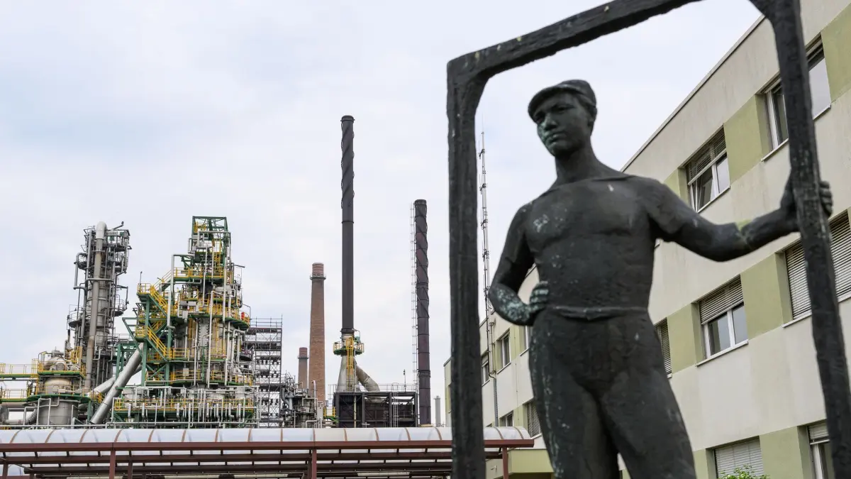 Raffinerie PCK: 11.05.2026, Brandenburg, Schwedt/Oder: Eine Bronzeskulptur eines Arbeiters steht vor Anlagen der Rohölverarbeitung auf dem Gelände der Raffinerie PCK. Am selben Tag besuchte Katherina Reiche (CDU), Bundeswirtschaftsministerin, das Unternehmen. Die Raffinerie in Schwedt versorgt weite Teile des Nordostens Deutschlands und Berlins mit Sprit, Heizöl und Kerosin. Russland hatte zum 1. Mai angekündigt an, dass die Durchleitung des Rohöls durch die Druschba-Pipeline gestoppt wird. Foto: Patrick Pleul/dpa - ACHTUNG: Nur zur redaktionellen Verwendung im Zusammenhang mit der aktuellen Berichterstattung +++ dpa-Bildfunk +++