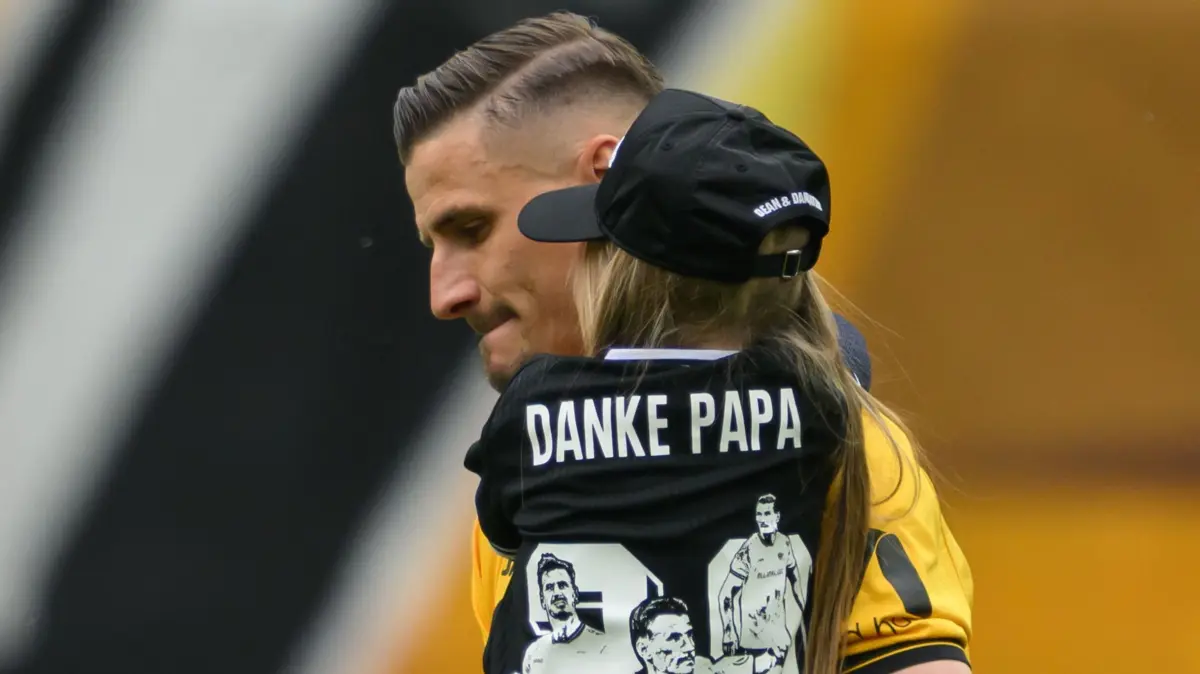 SG Dynamo Dresden - Holstein Kiel: 17.05.2026, Sachsen, Dresden: Fußball, Männer: 2. Bundesliga, SG Dynamo Dresden - Holstein Kiel, 34. Spieltag, Rudolf-Harbig-Stadion, Stefan Kutschke (Dynamo Dresden) kommt mit seiner Tochter zu seiner Verabschiedung aufs Feld - auf der Rückseite ihres T-Shirts steht «Danke Papa». Foto: Robert Michael/dpa - WICHTIGER HINWEIS: Gemäß den Vorgaben der DFL Deutsche Fußball Liga bzw. des DFB Deutscher Fußball-Bund ist es untersagt, in dem Stadion und/oder vom Spiel angefertigte Fotoaufnahmen in Form von Sequenzbildern und/oder videoähnlichen Fotostrecken zu verwerten bzw. verwerten zu lassen. +++ dpa-Bildfunk +++