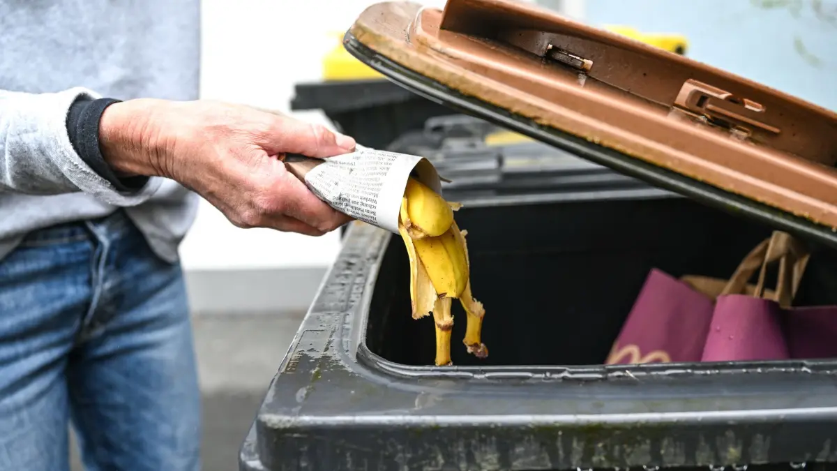 Eine Frau wirft Bananenschalen in den Biomüll: ARCHIV - Nur in kleinen Mengen ein Fall für den Kompost: Wer sichergehen will, wirft Bananenschalen lieber in die Biotonne. (zu dpa: «Kompost oder Biotonne: Welcher Abfall gehört wohin?») Foto: Felix Kästle/dpa - Honorarfrei nur für Bezieher des dpa-Themendienstes +++ dpa-Themendienst +++
