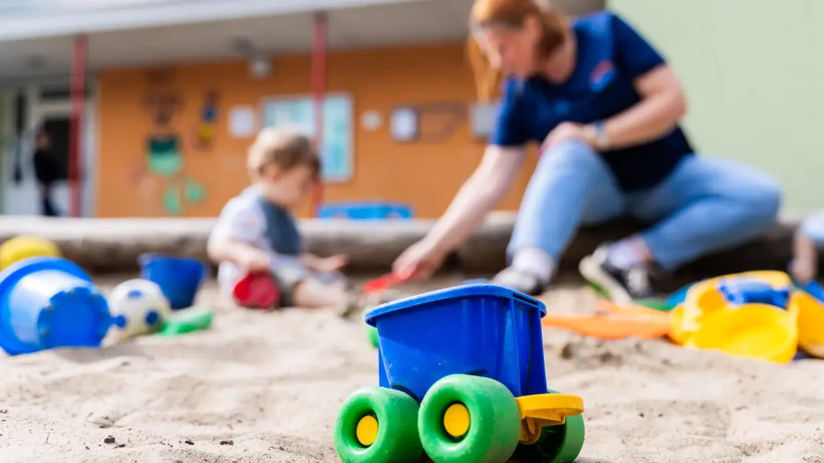Ein Kind spielt mit einer Erzieherin im Sandkasten einer Kita. Die hochumstrittenen Lockerungen der Personalvorgaben in nordrhein-westfälischen Kitas können ab sofort umgesetzt werden. (zu dpa: «Umstrittene Kita-Personalverordnung in Kraft») +++ dpa-Bildfunk +++