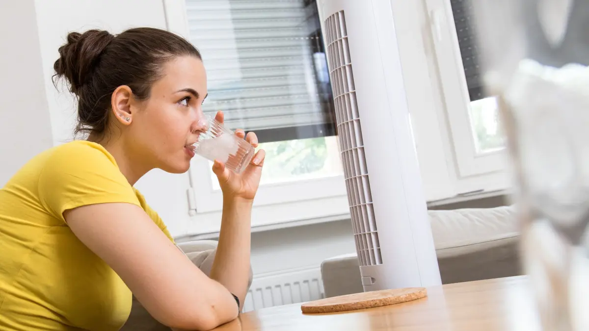 Eine Frau kühlt sich mit Wasser und Ventilator ab