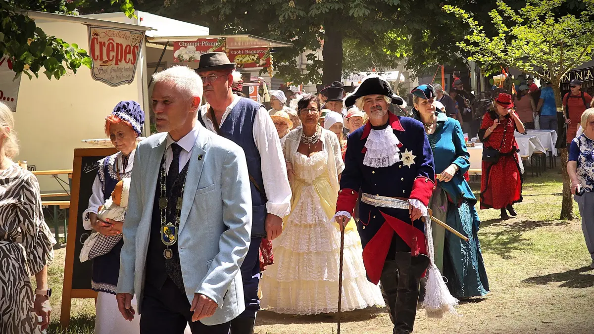 Das Heimafest in Erkner 2026. Bürgermeister Henryk Pilz führt den Zug durch den Rathauspark an. Direkt hinter ihm die ersten Bürger der Stadt, Fischer Hans Hans und seine Frau, die gerade symbolisch am Dämeritzsee angelegt haben und viele weitere kostümierte Mitglieder des Heimatvereins Erkner.