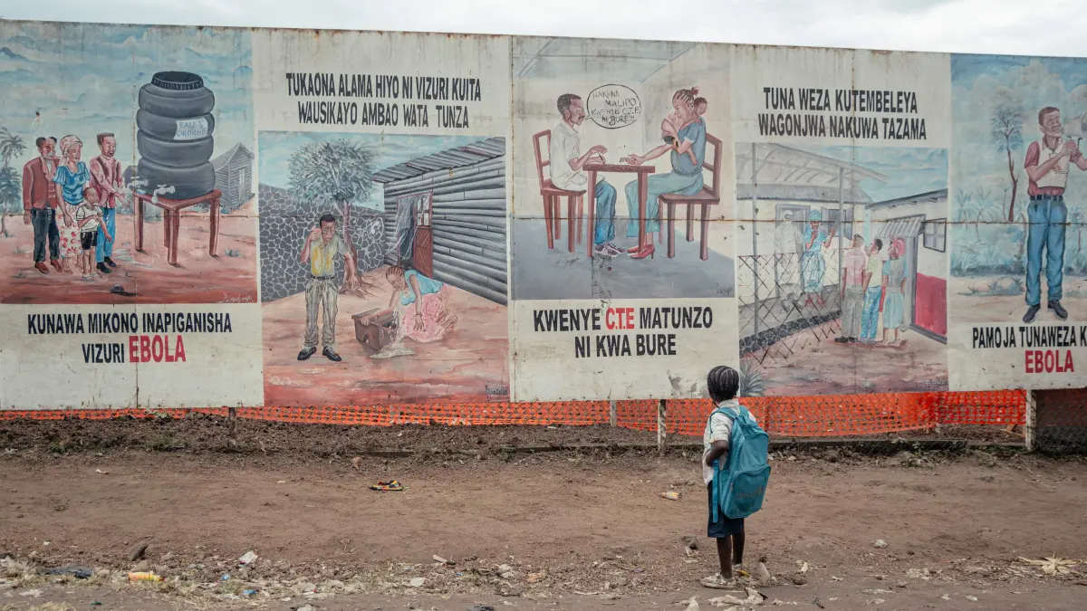 A child returning from school stops to look at Ebola awareness illustrations displayed on the signboards of the Ebola Treatment Center (ETC) in Munigi on June 2, 2026. The sole airport providing humanitarian organisations access to the epicentre of an Ebola outbreak in the Democratic Republic of Congo reopened on June 2, 2026, when the reported number of suspected cases declined.
The country of 100 million people declared on May 15 that it was battling a major epidemic of the highly contagious haemorrhagic fever, prompting the World Health Organization to issue an international health alert. (Photo by Jospin Mwisha / AFP)
