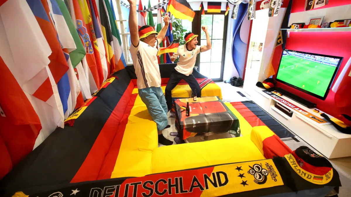 ILLUSTRATION - Die beiden FußballfansStefan (r) und Wolla jubeln am 16.06.2016 in ihrem dekorierten Wohnzimmer in Haan (Nordrhein-Westfalen) schon mal zur Probe. Das gleichgeschlechtliche Paar hat alle Fahnen der 24 teilnehmenden Mannschaften aufgehängt und verfolgen möglichst alle Spiele am Fernseher. Foto: Roland Weihrauch/dpa ++ +++ dpa-Bildfunk +++