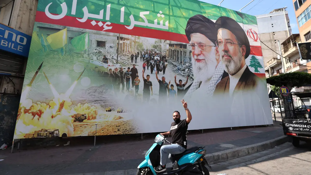 A on his moped flashes the V-sign for victory as he stops in front of a giant billboard depicting the late Iranian leader Ayatollah Ali Khamenei C), and Iranian Supreme Leader Ayatollah Mojtaba Khamenei, with Arabic writing that reads: "Thank you Iran", in Dahiyeh, Beirut's southern suburbs on June 15, 2026. Hezbollah thanked its backer Iran on June 15, for insisting that Lebanon, where Israel and the militants have been at war, be included in the deal to end the Middle East conflict. Lebanon was drawn into the Middle East war on March 2 when Tehran-backed militant group Hezbollah launched attacks on Israel to avenge the killing of the Iranian leader. Israel has responded with broad strikes across Lebanon and a ground offensive. (Photo by Anwar AMRO / AFP) /