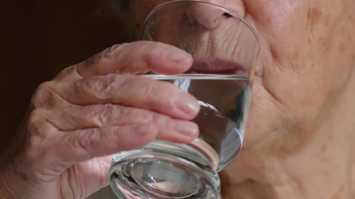 Ältere Frau trinkt ein Glas Wasser: ILLUSTRATION - Weil älteren Menschen oft das Durstgefühl fehlt, ist es gut, sie regelmäßig ans Trinken zu erinnern. (zu dpa: «Hitze setzt Pflegebedürftigen zu: 6 Tipps für Angehörige») Foto: Sebastian Willnow/dpa-tmn - Honorarfrei nur für Bezieher des dpa-Themendienstes +++ dpa-Themendienst +++