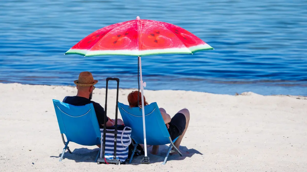 Hitze in Mecklenburg-Vorpommern: 24.06.2026, Mecklenburg-Vorpommern, Kühlungsborn: Unter einem Sonnenschirm sitzen Urlauber bei hochsommerlichem Wetter am Ostseestrand. Auch für die kommenden Tage hat der Deutsche Wetterdienst (DWD) für Norddeutschland weiterhin Sonnenschein und Temperaturen bis zu 38 Grad angekündigt. Foto: Jens Büttner/dpa +++ dpa-Bildfunk +++