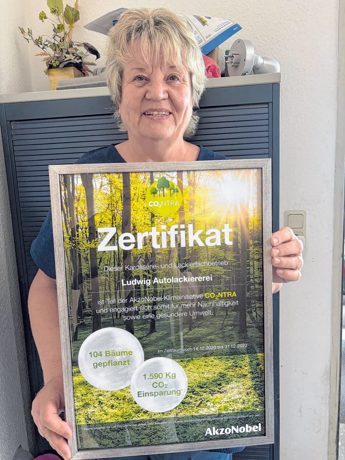 Stolz auf das Umweltzertifikat: Petra Ludwig zeigt die Urkunde, die bestätigt, dass die Letschiner Autolackiererei als Teil der AkzoNobel-Klimainitiative CO2NTRA für Nachhaltigkeit und eine gesündere Umwelt engagiert.