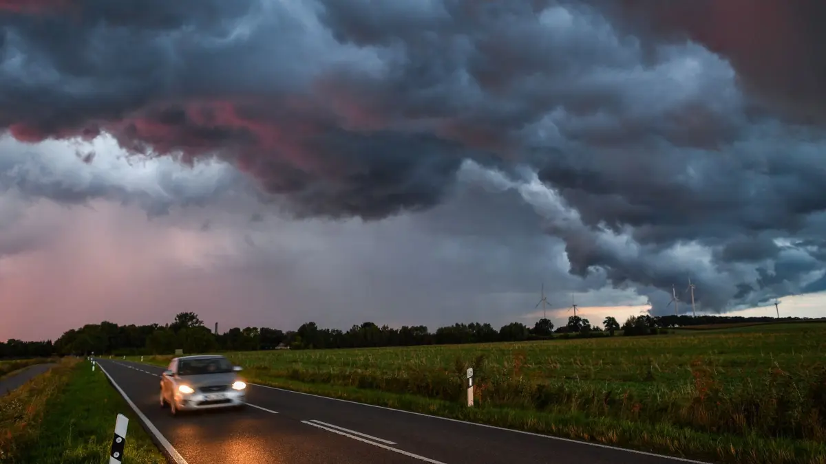 Gewitterzelle zieht im Sonnenuntergang über eine Landstraße: ARCHIV - Unwetter im Anmarsch: Nun ist höchste Aufmerksamkeit gefragt. (zu dpa: «Sicher im Auto bei Gewitter – worauf es jetzt ankommt») Foto: Patrick Pleul/dpa/dpa-tmn - Honorarfrei nur für Bezieher des dpa-Themendienstes +++ dpa-Themendienst +++