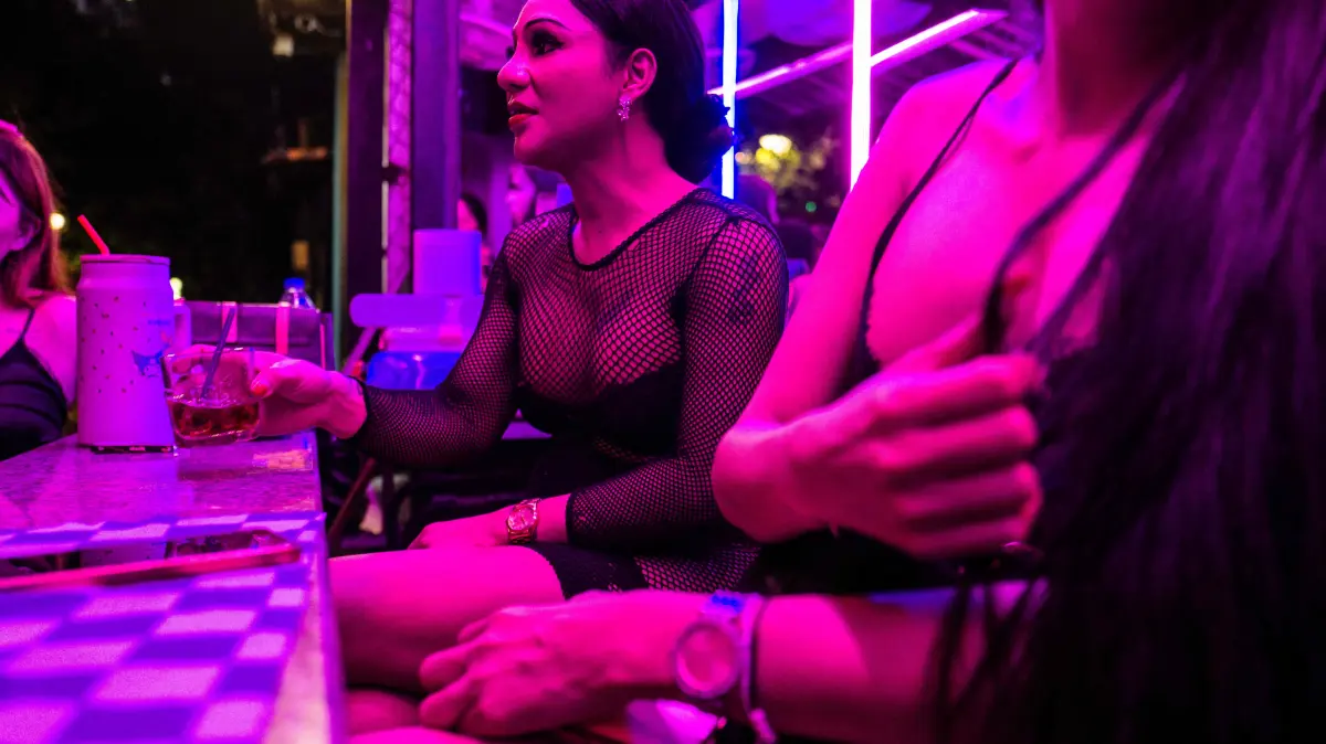 THAILAND-AUSTRALIA-CRIME-TOURISM-PROSTITUTION: Emily (C), a sex worker, sits with her colleagues as they wait for clients in the back of a bar in Pattaya on July 2, 2026. Scantily dressed and wearing stiletto heels, hundreds of girls, some apparently very young, form a seedy guard of honour under the lights of Soi 6, a street in one of Pattaya's red-light districts. (Photo by ANTHONY WALLACE / AFP) / TO GO WITH: Thailand-Australia-crime-tourism-prostitution