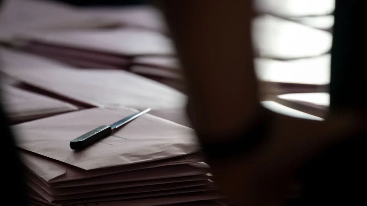 Neuwahl in Wülfershausen: ARCHIV - 08.03.2026, Bayern, Untermerzbach: Wahlhelfer stehen vor Stapeln mit Wahlbriefen für die Briefwahl, auf denen ein Brieföffner liegt. (zu dpa: «Nach Wahlfälschung im Dorf Neuwahl von Bürgermeister») Foto: Pia Bayer/dpa +++ dpa-Bildfunk +++