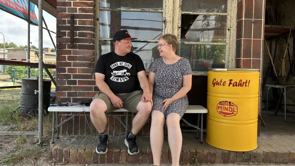 Jens und Sophie Jäger aus Friedersdorf bei Königs Wusterhausen sitzen vor dem ehemaligen Kassenhäuschen der alten Minol-Tankstelle. Zusammen mit ihrem Verein restaurieren sie das DDR-Relikt. Dabei gab es kürzlich einen spektakulären Fund.