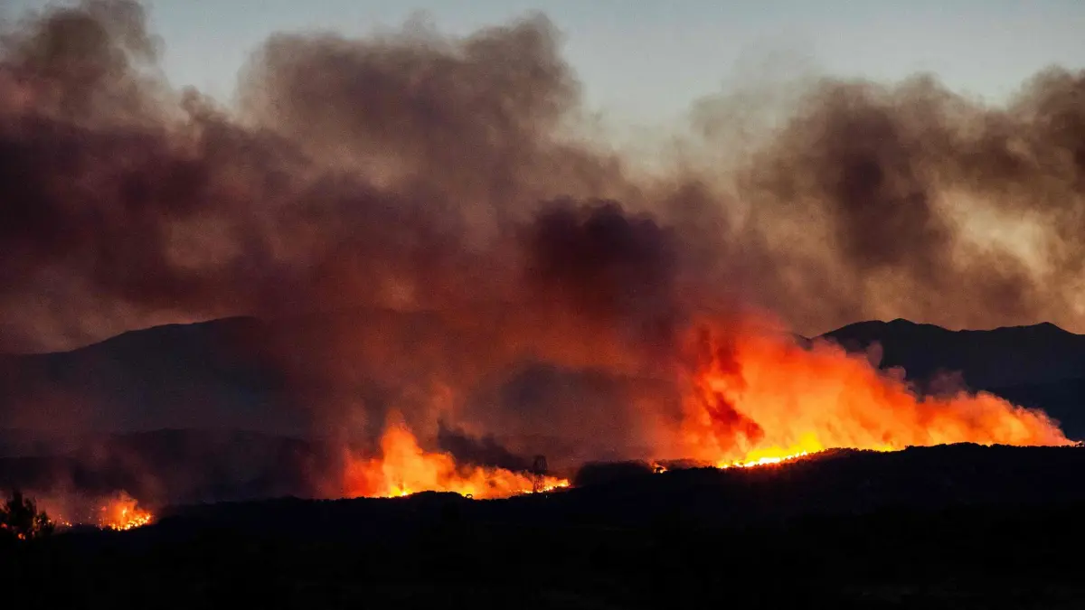 Waldbrände in Südfrankreich: 05.07.2026, Frankreich, Millas: Qualmwolken eines Waldbrandes in der Region Aspres verdunkeln den Himmel. Am Vortag gegen 19:30 Uhr brach in einem schwer zugänglichen Gebirgsmassiv in der Nähe von Trevillach im Departement Pyrénées-Orientales in Südfrankreich ein Waldbrand aus, der sich über Nacht rasch ausbreitete. Derzeit werden mehr als 10.000 Einwohner evakuiert, da sich der Waldbrand rasch ausbreitet und bereits rund 2.000 Hektar verwüstet hat. Foto: Jc Milhet/AFP/dpa +++ dpa-Bildfunk +++