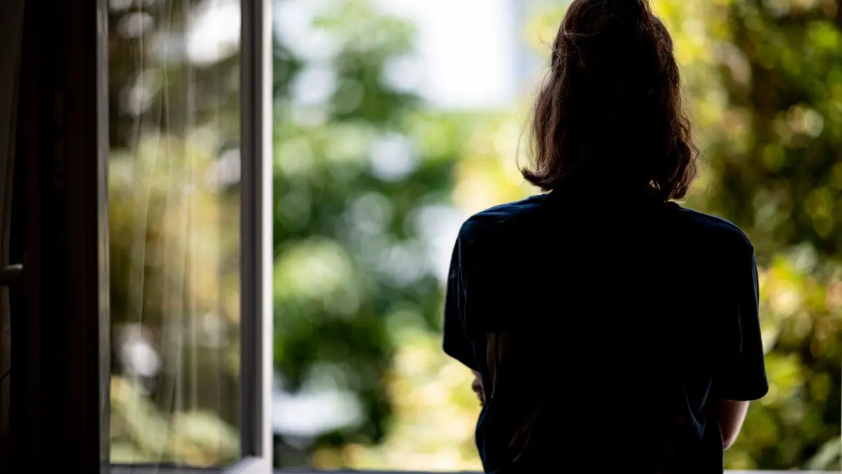 Symbolbild - Depression: ARCHIV - 13.07.2021, Berlin: Eine junge Frau steht in ihrer Wohnung an einem Fenster. (zu dpa: «Umfrage: Menschen in Deutschland leiden enorm unter Hitze») Foto: Fabian Sommer/dpa +++ dpa-Bildfunk +++