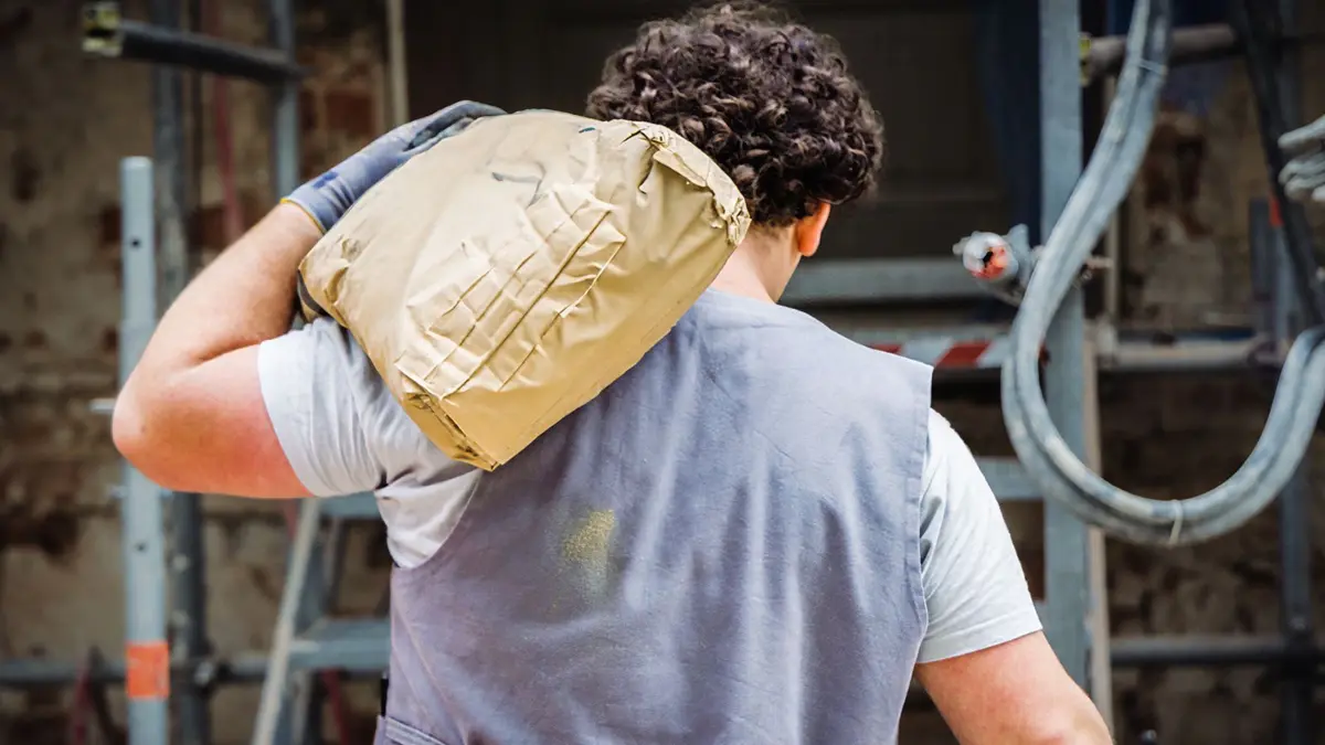 Ein junger Mann schleppt einen Sack mit Baumaterialien auf einer Baustelle