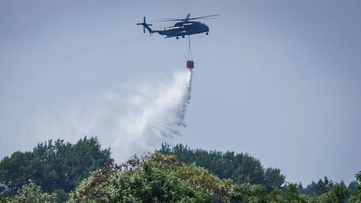 Waldbrand im Müritz-Nationalpark: 16.07.2026, Mecklenburg-Vorpommern, Kratzeburg: Ein Bundeswehr-Hubschrauber CH-53 wirft aus dem 5000-Liter-Tank Löschwasser über dem Waldbrand im Müritz-Nationalpark ab. Der Großbrand auf einem ehemaligen Truppenübungsgelände hat sich auf mittlerweile 269 Hektar ausgedehnt. Derzeit sind etwa 375 Einsatzkräfte vor Ort. Foto: Jens Büttner/dpa +++ dpa-Bildfunk +++